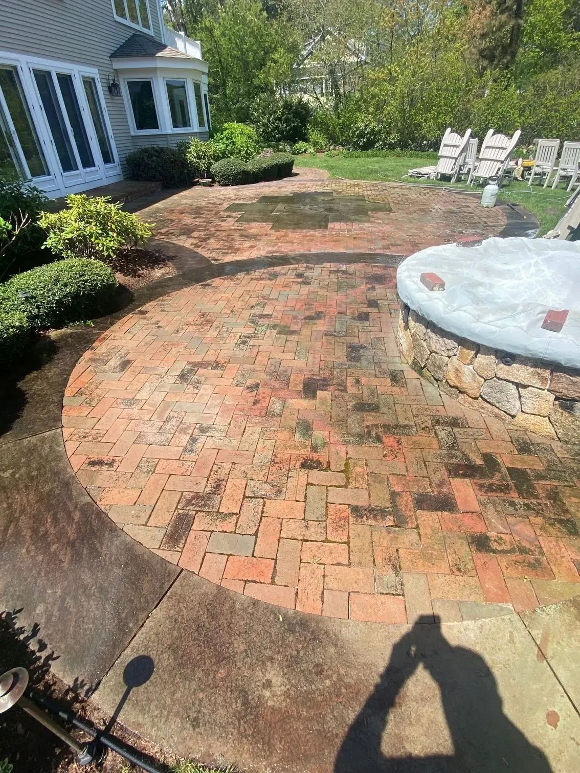 Brick patio with circular design, near a house and greenery; some wet spots.