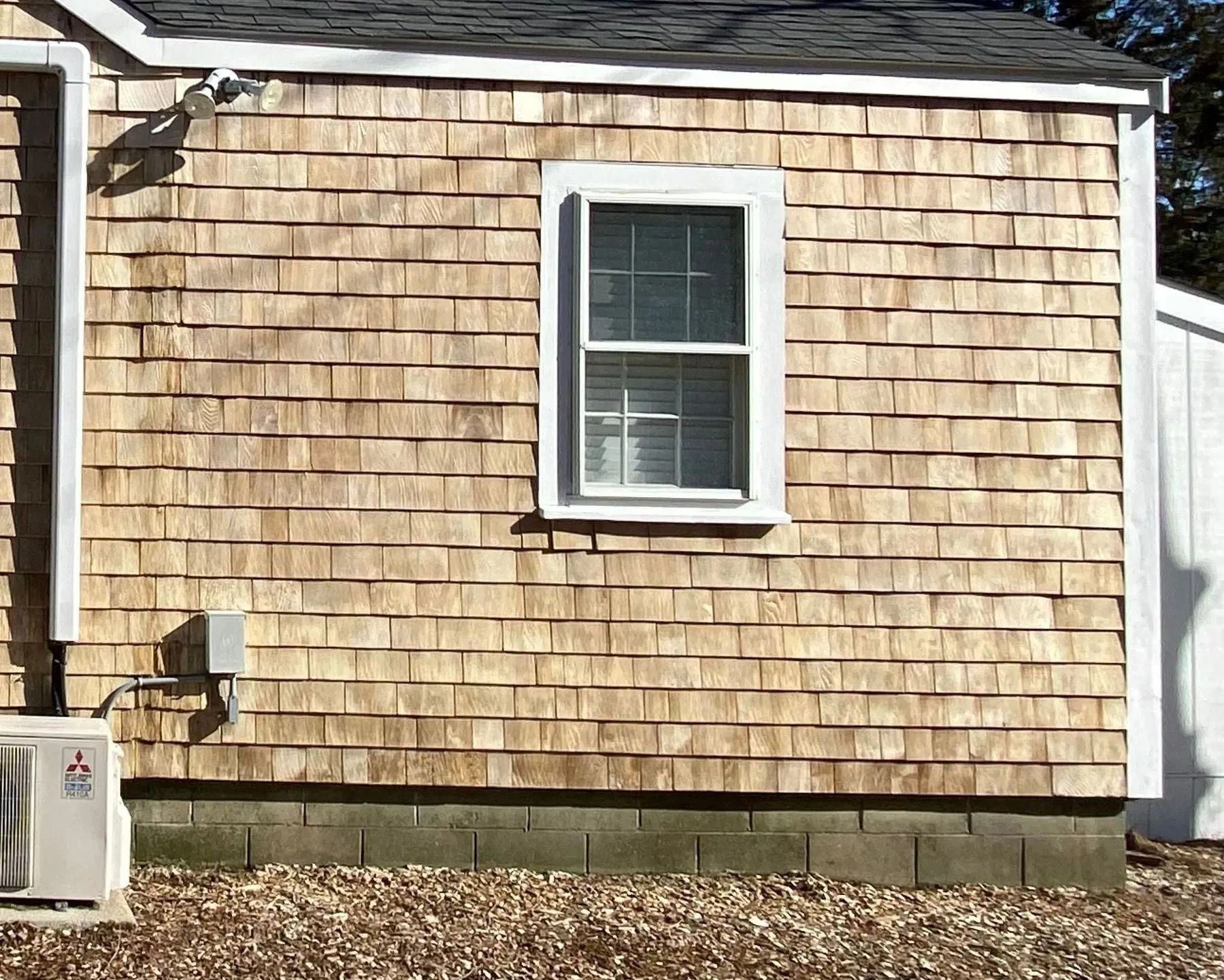 Exterior of a building with weathered wood shingle siding, a window, and an AC unit.