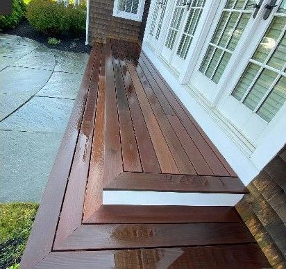 Wooden deck with steps next to a house with white French doors; wet surface.
