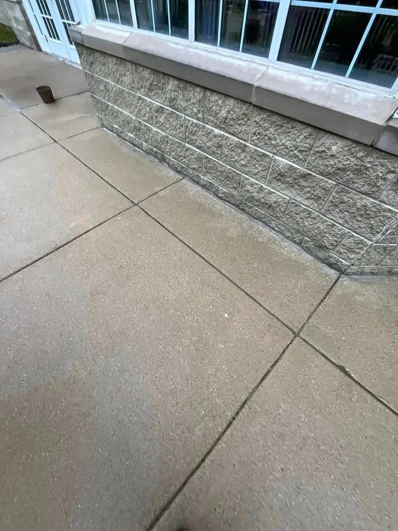 A concrete sidewalk next to a brick wall and a window.