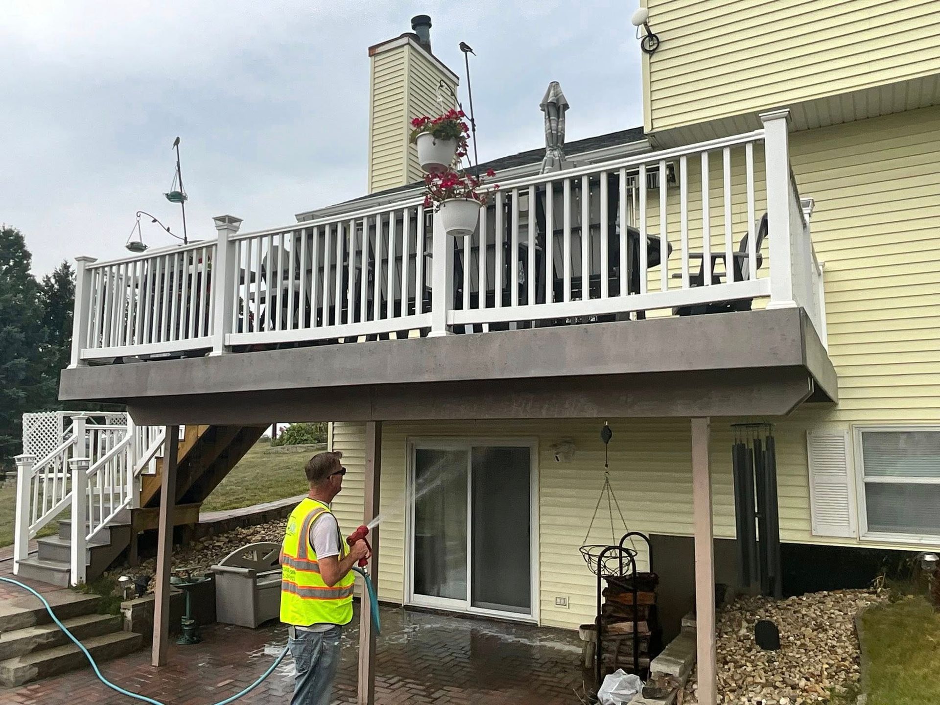 A man in a yellow vest is spraying water on a deck.