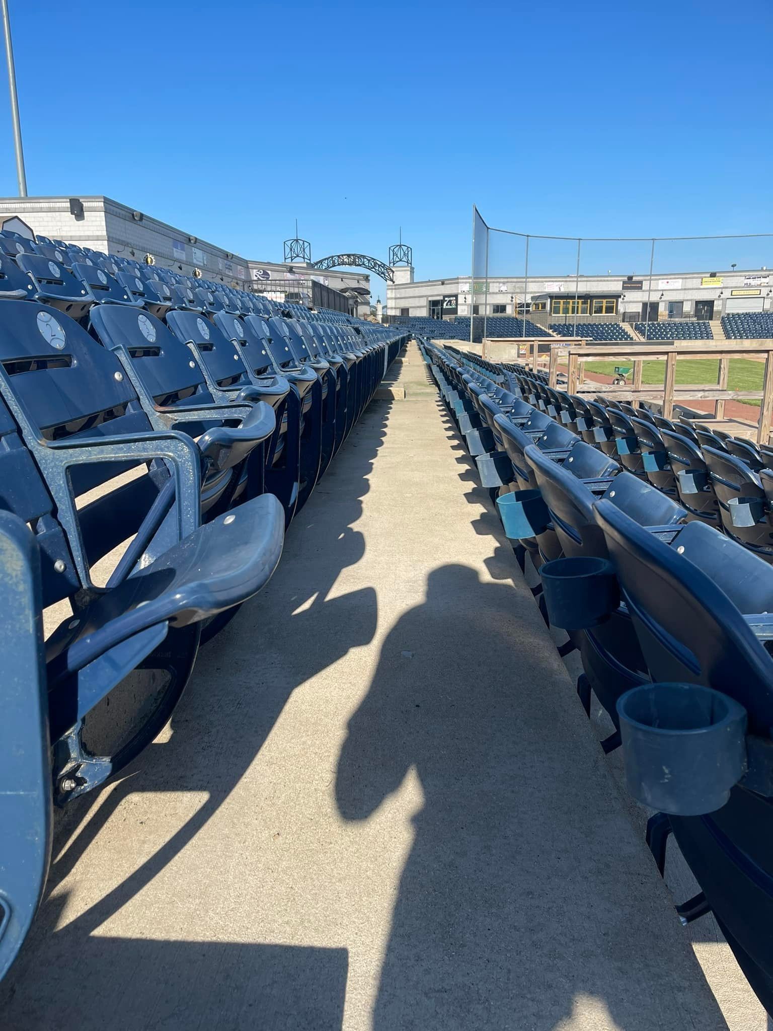 A row of empty stadium seats with a person 's shadow on the ground.