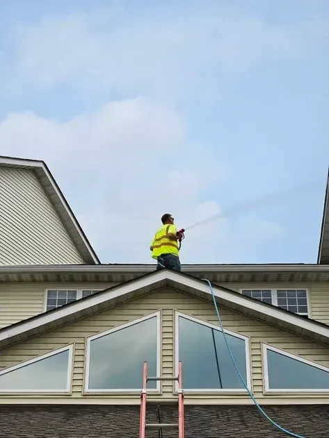 A man is cleaning the roof of a house with a hose.