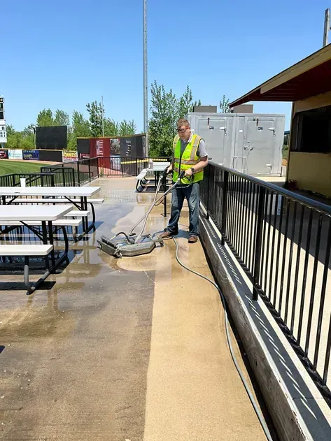 A man in a yellow vest is cleaning a patio with a machine.