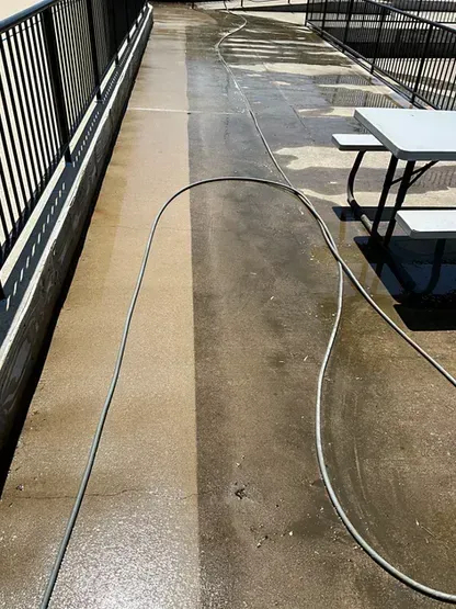 A hose is being used to clean a concrete walkway next to a picnic table.