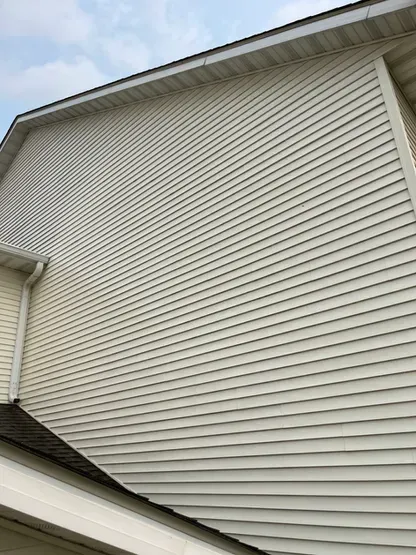 The side of a house with white siding and a roof.