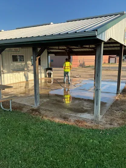 A man is cleaning a concrete floor under a covered area.