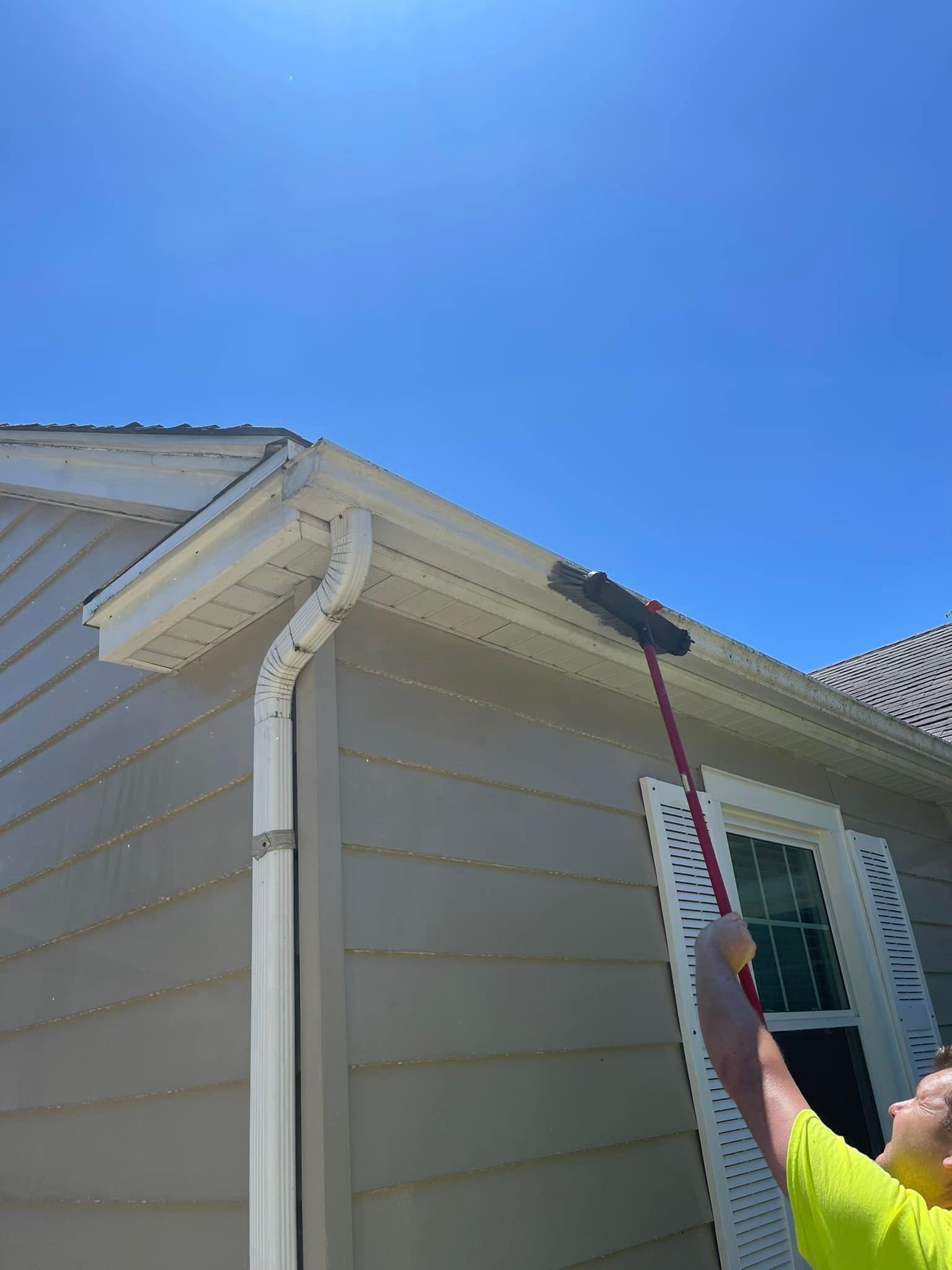 A man is cleaning the gutters of a house with a broom.