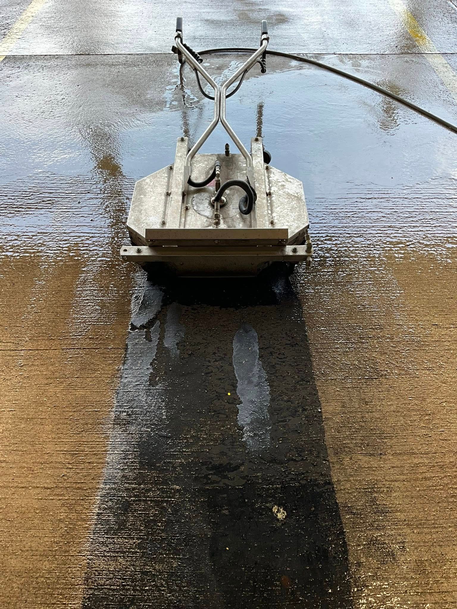 A machine is cleaning a concrete surface with a hose.