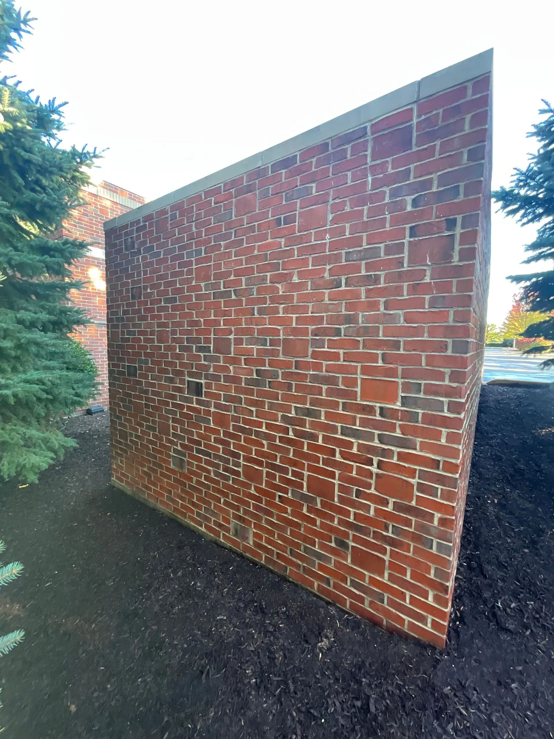 A large brick wall is surrounded by trees and dirt.