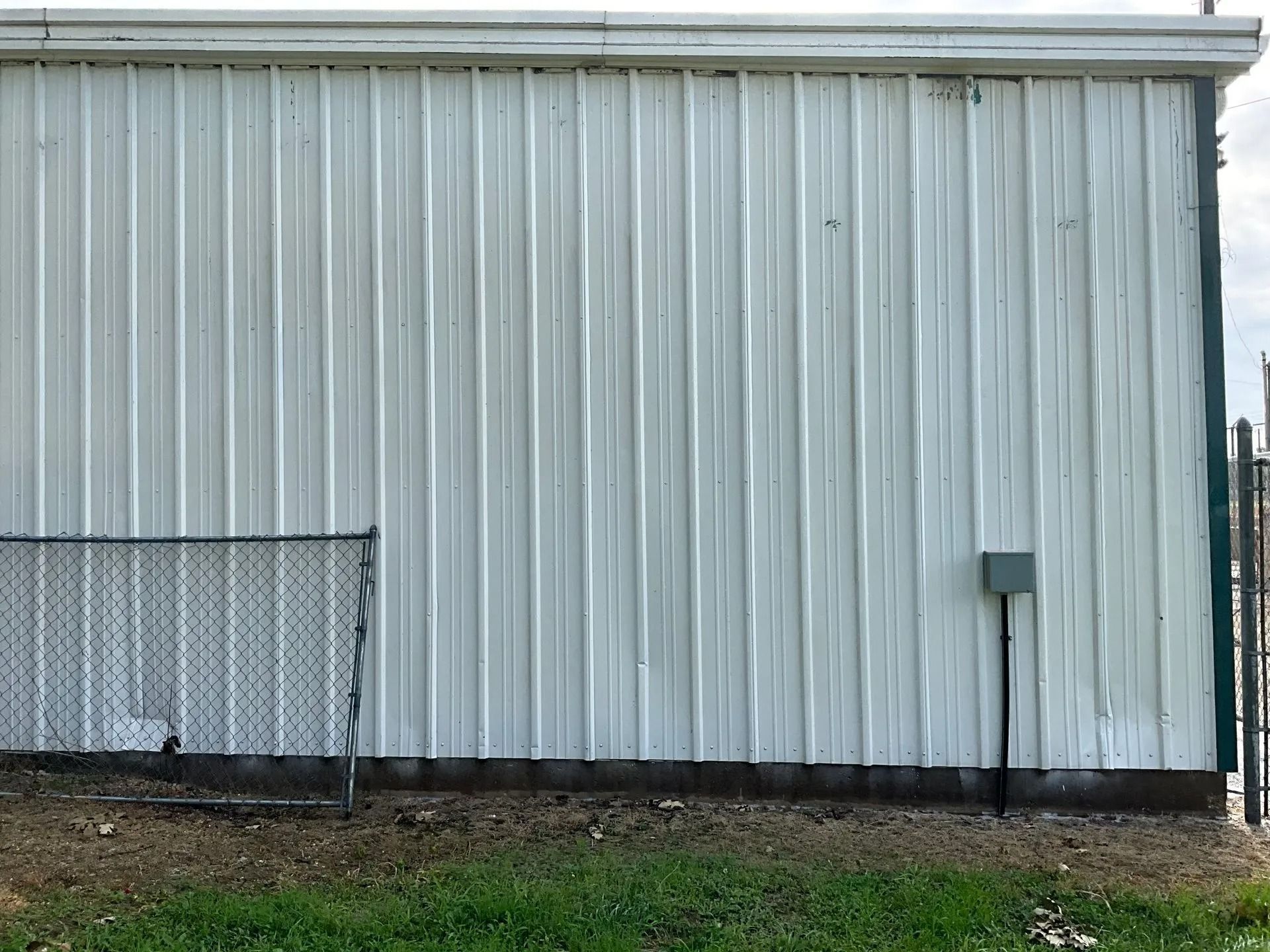 A white metal building with a green fence in front of it.