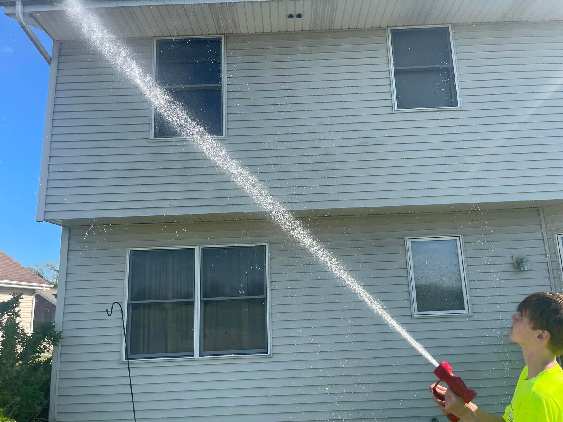 A man is spraying water from a hose in front of a house.