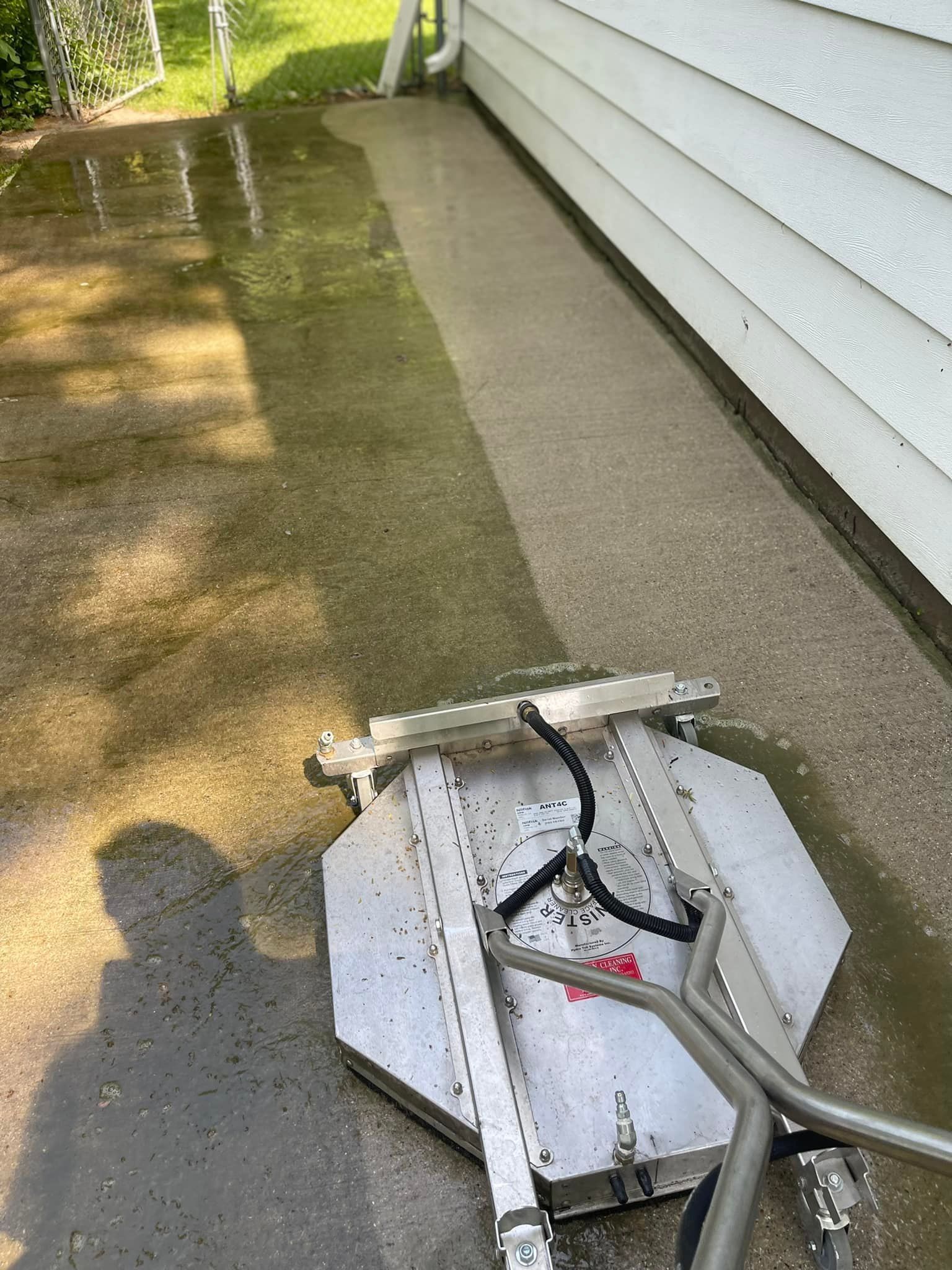 A machine is cleaning a concrete driveway next to a house.