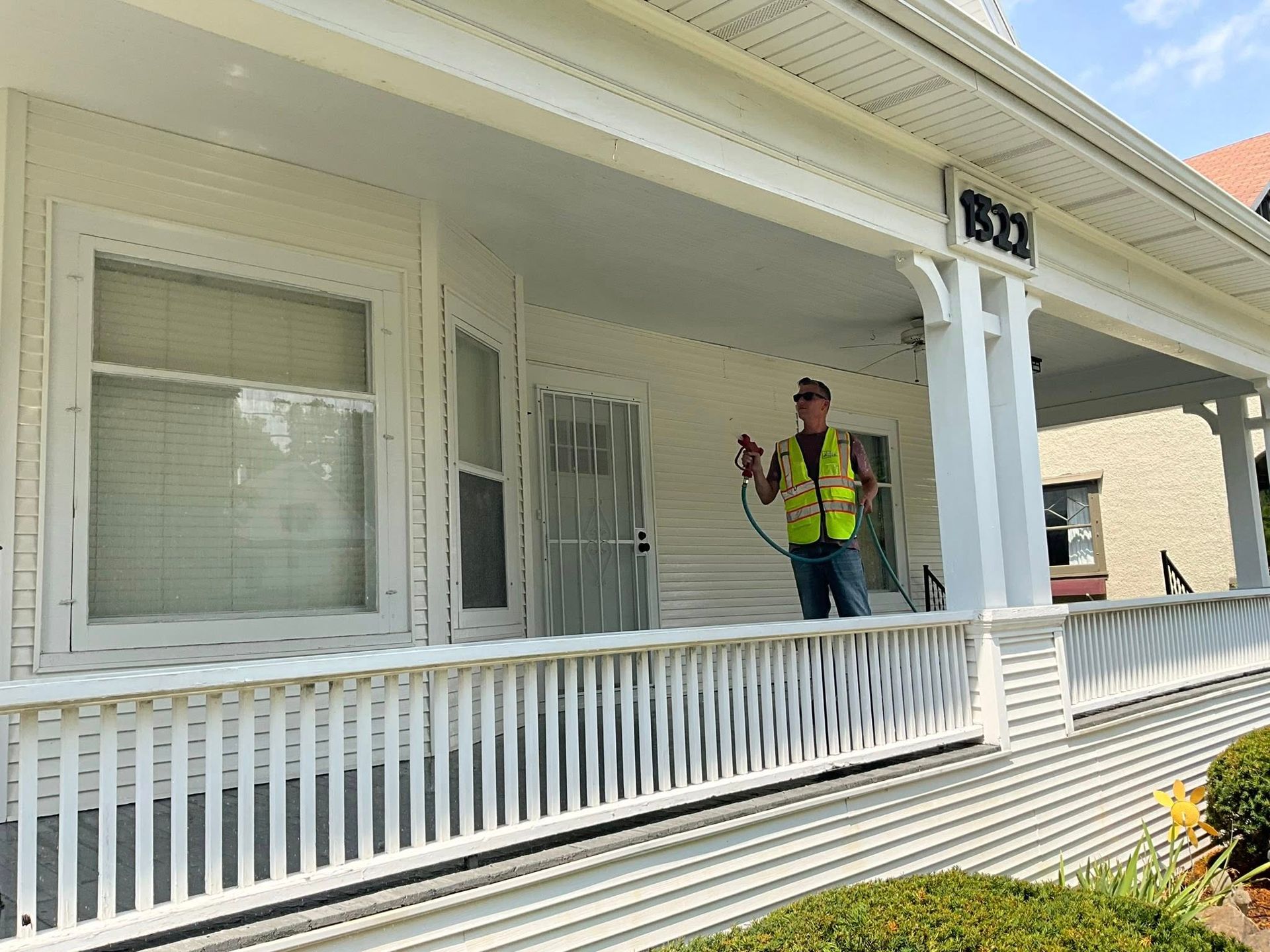 A man in a yellow vest is standing on the porch of a white house.