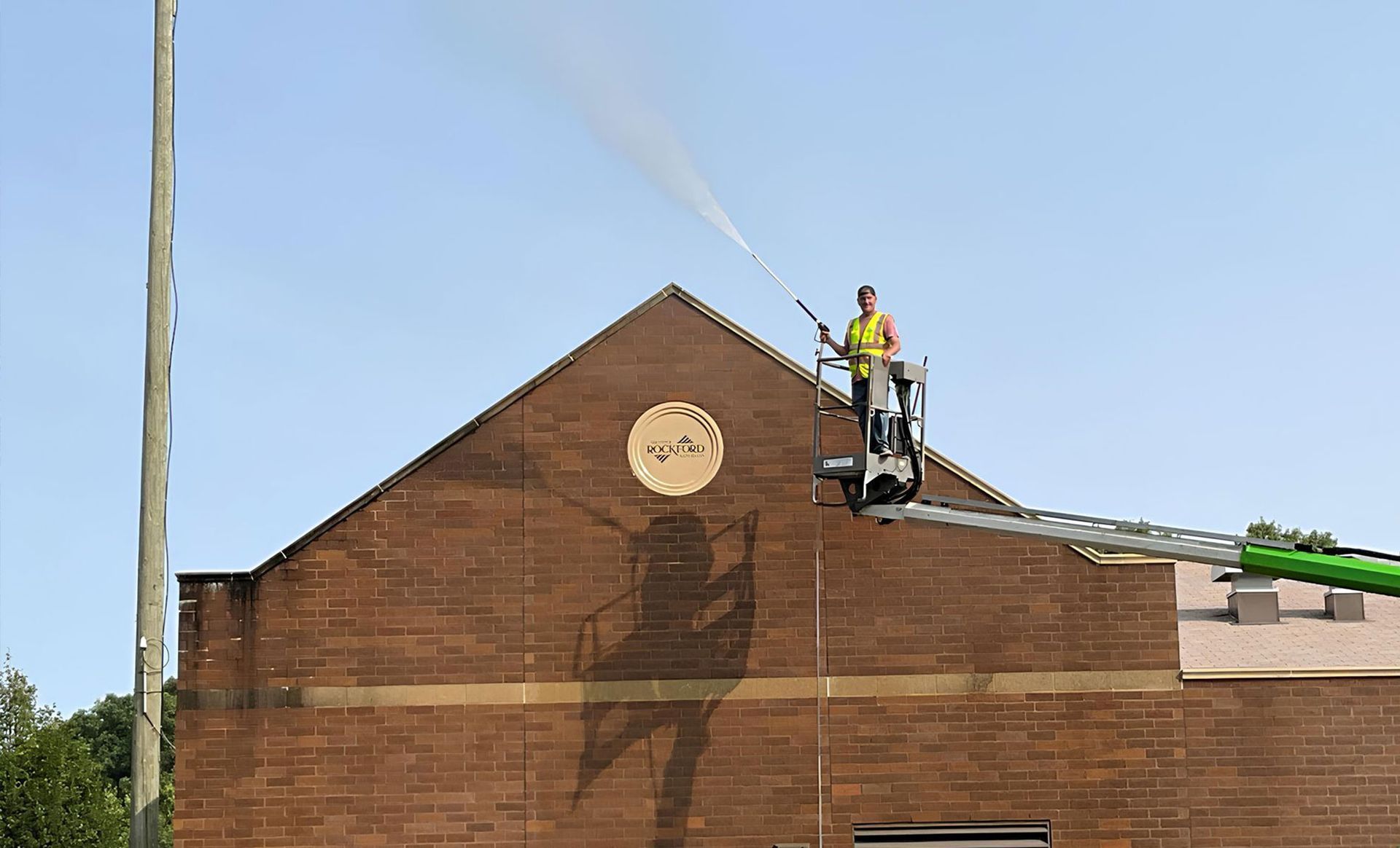 A man is standing on a crane spraying water on a brick building.