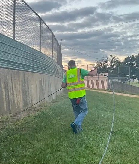 A man in a yellow vest is walking in the grass with a hose.