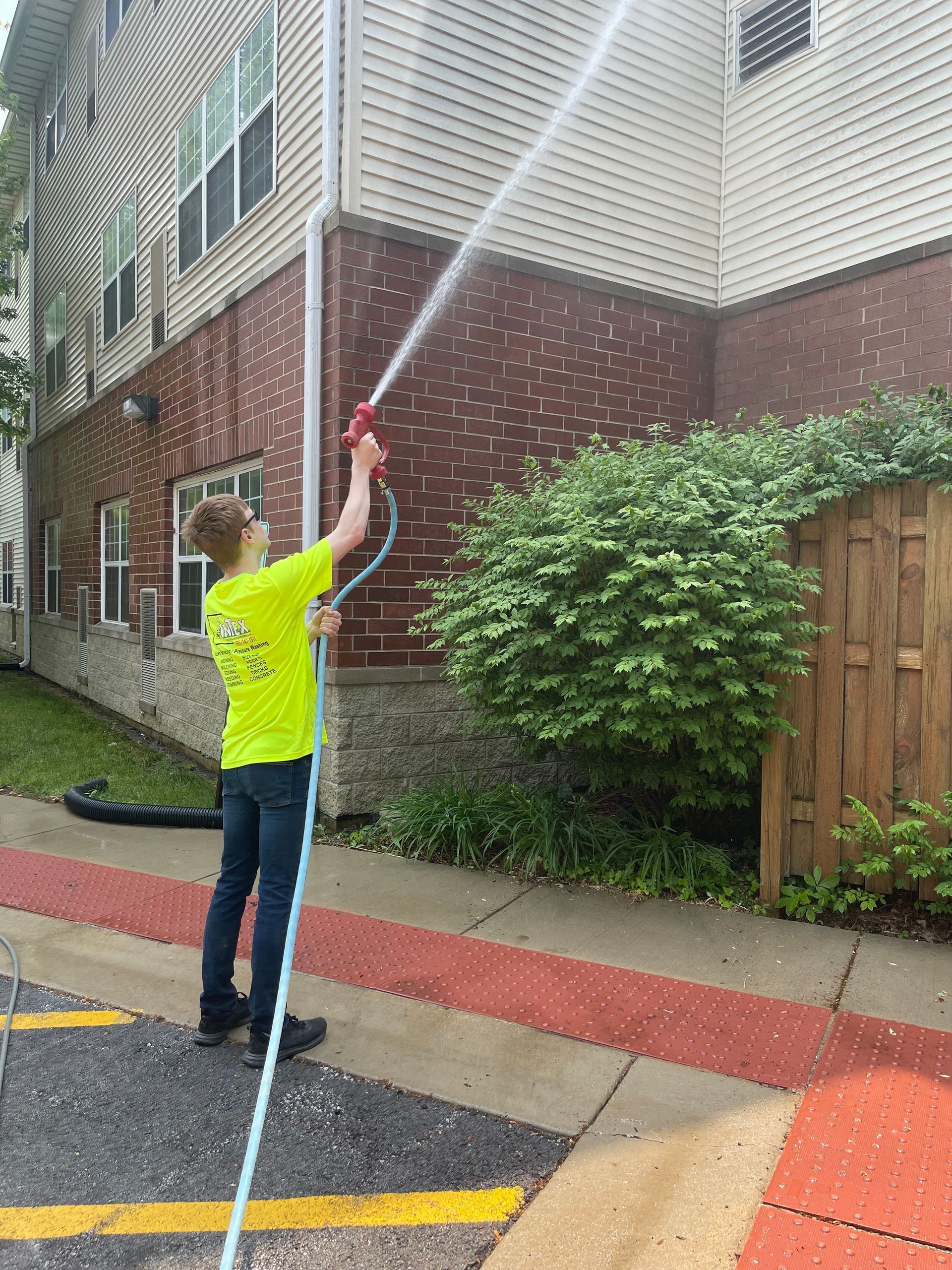 A man is spraying water from a hose on the side of a building.