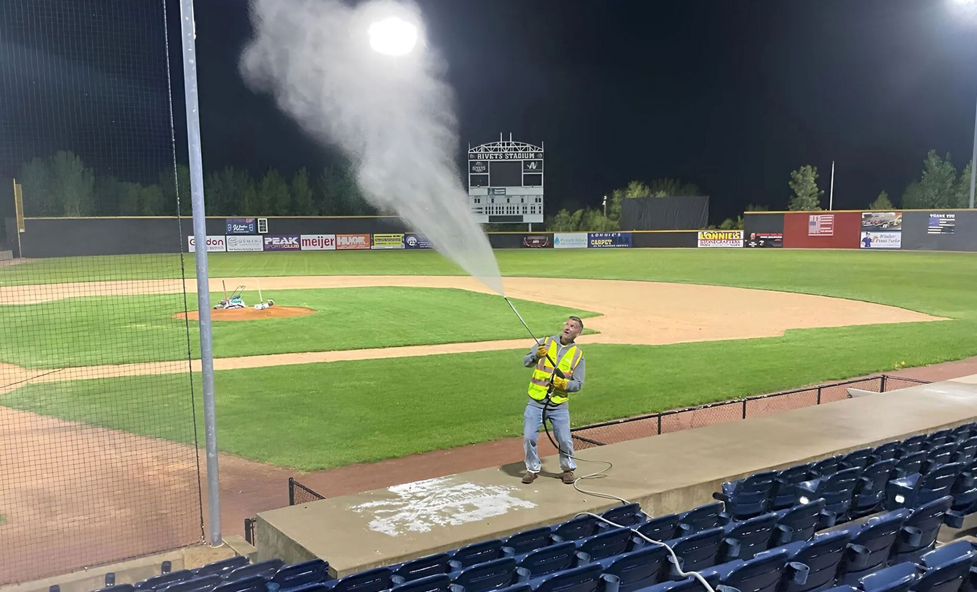 A man spraying water on a baseball field at night