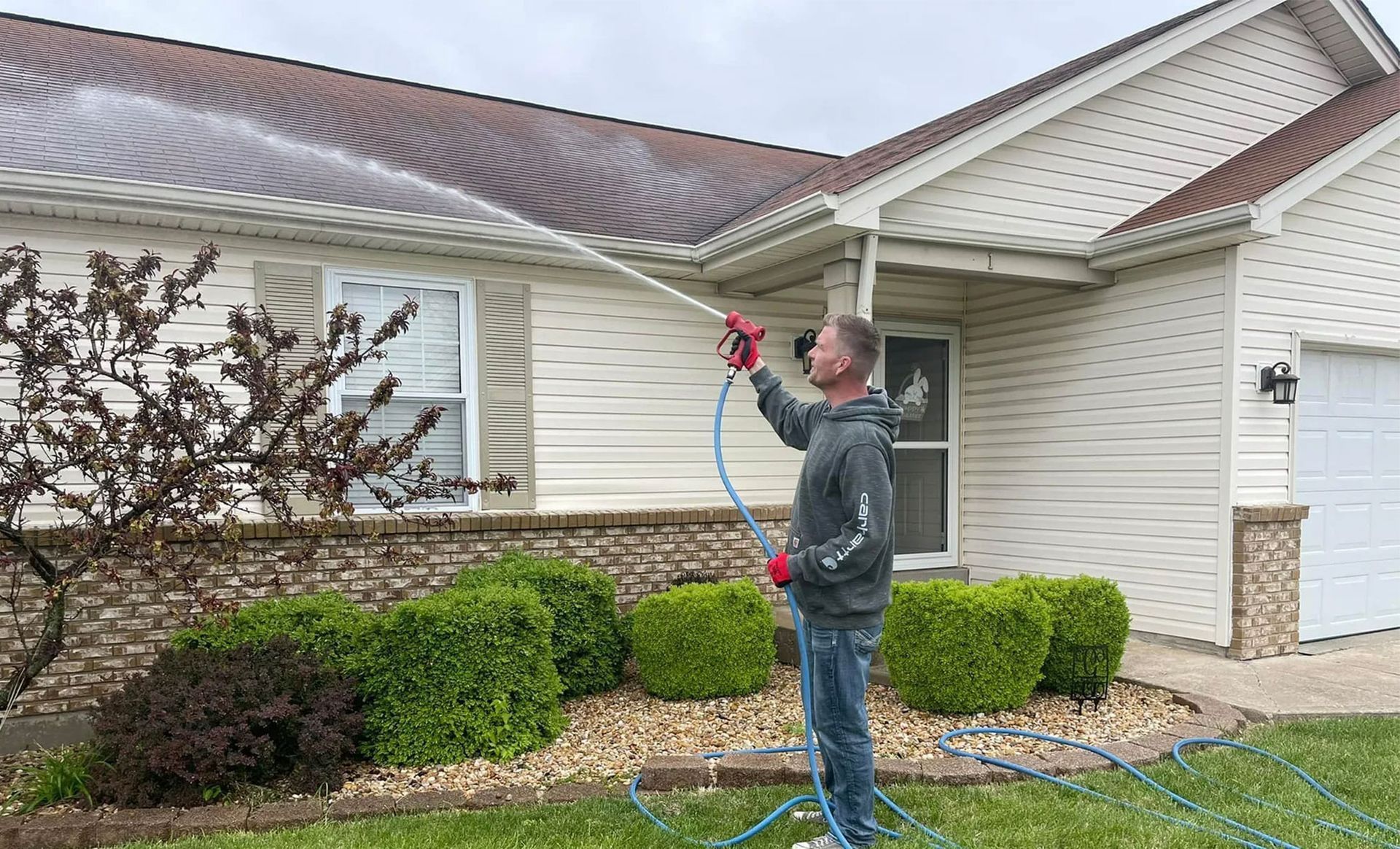 A man is cleaning the roof of a house with a pressure washer.