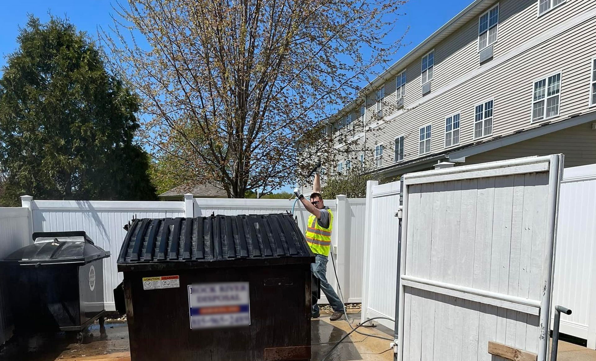 A man is standing next to a dumpster in front of a building.