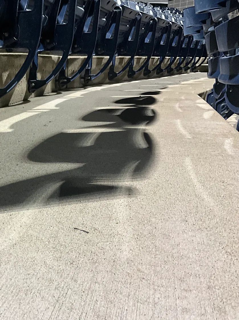 Row of dark, metal structures casting shadows on a light-colored concrete surface.
