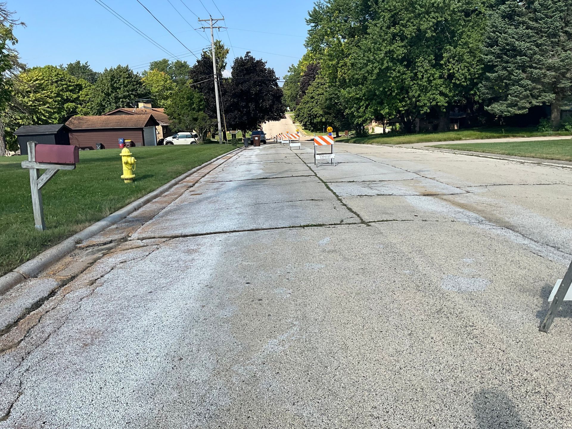 Damaged road with white powder, yellow fire hydrant, mailbox, trees, and houses in the background.