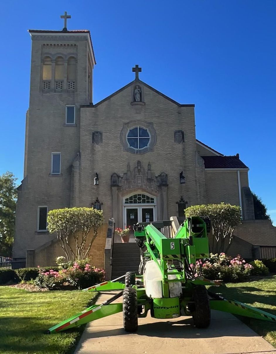 Green utility vehicle in front of a beige church with a cross on top and a clear blue sky.