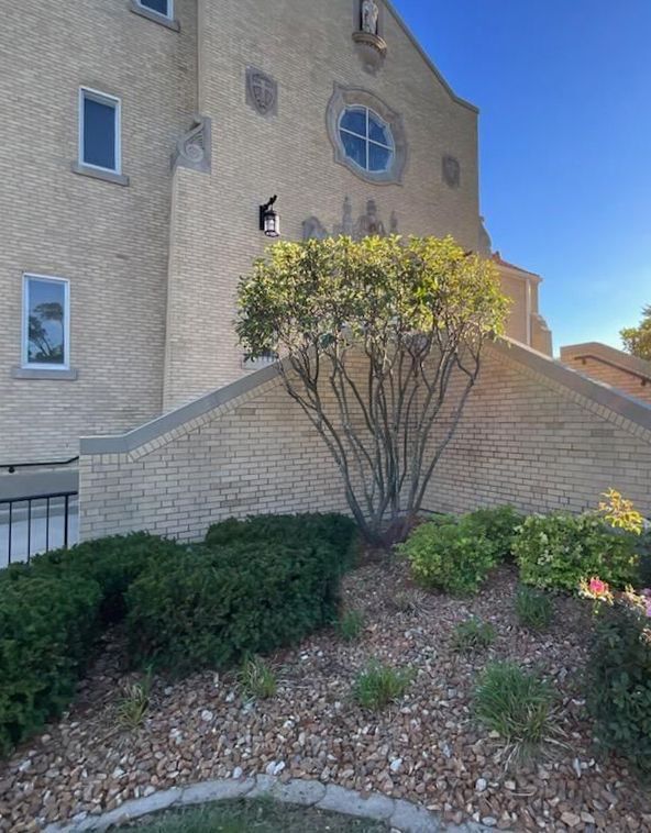 Tan brick building with shrubbery in front, clear blue sky.