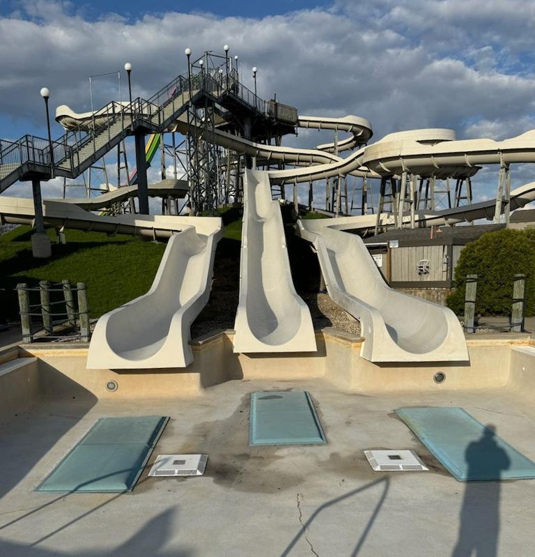 Empty water park; concrete slides lead into an empty pool. Cloudy sky overhead.
