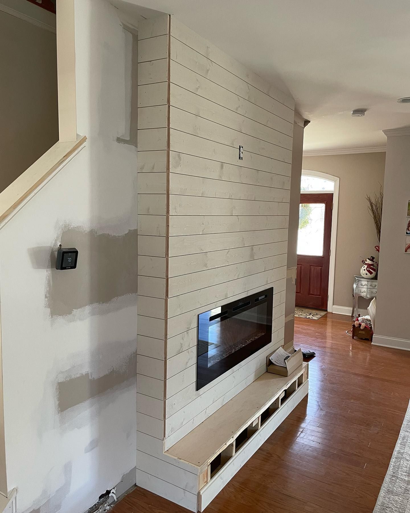 Fireplace wall under construction with light wood planks, a black fireplace, and a built-in bench.