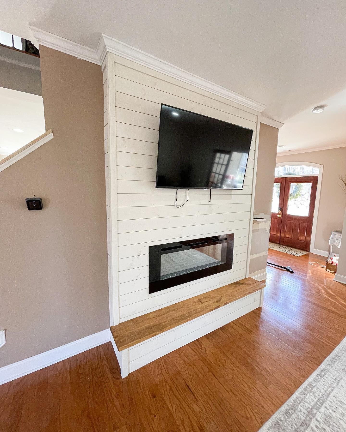 Fireplace with mounted TV and wooden bench in a living room; white paneling and hardwood floors.