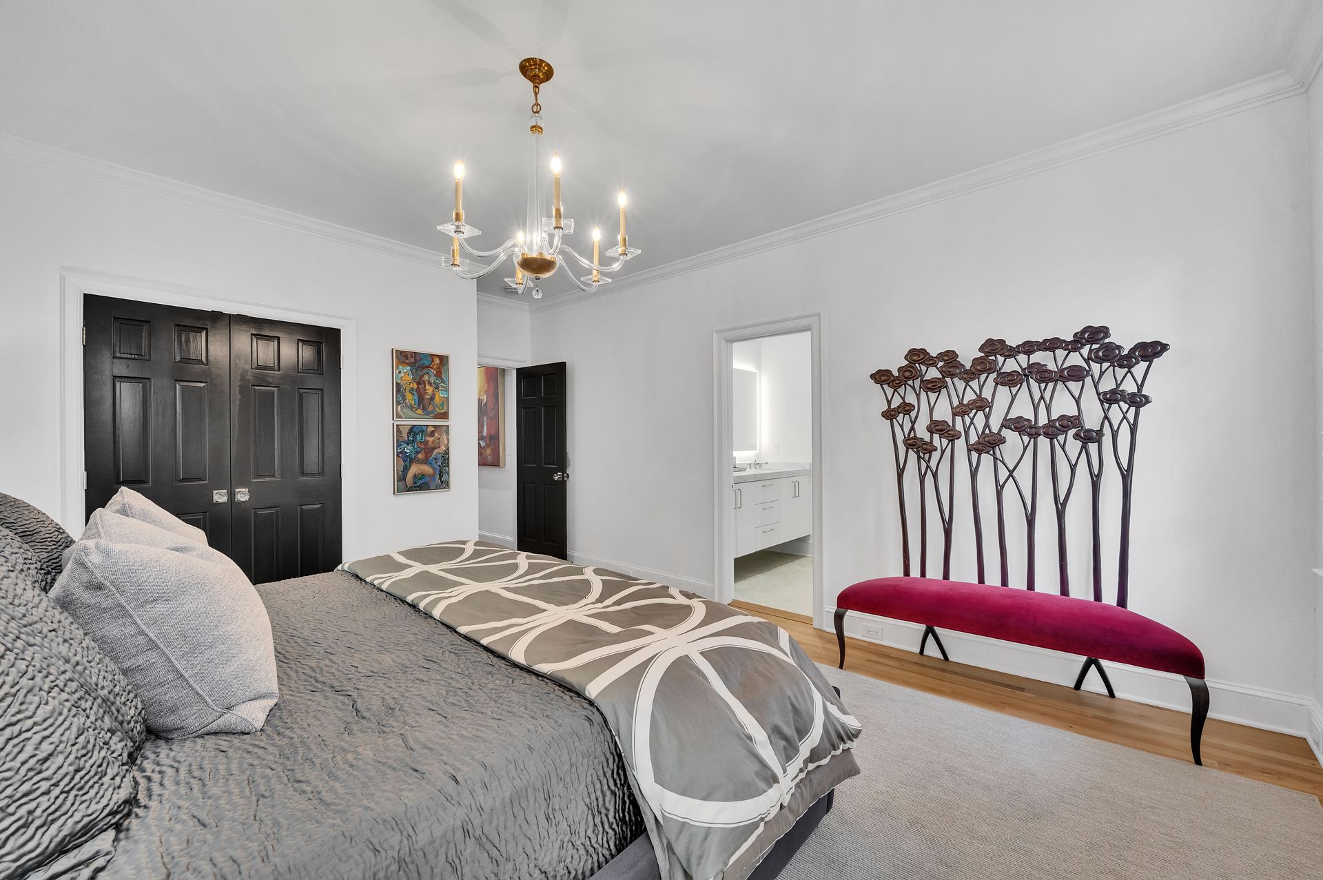 Bedroom with gray bed, black closet doors, chandelier, and a decorative bench.