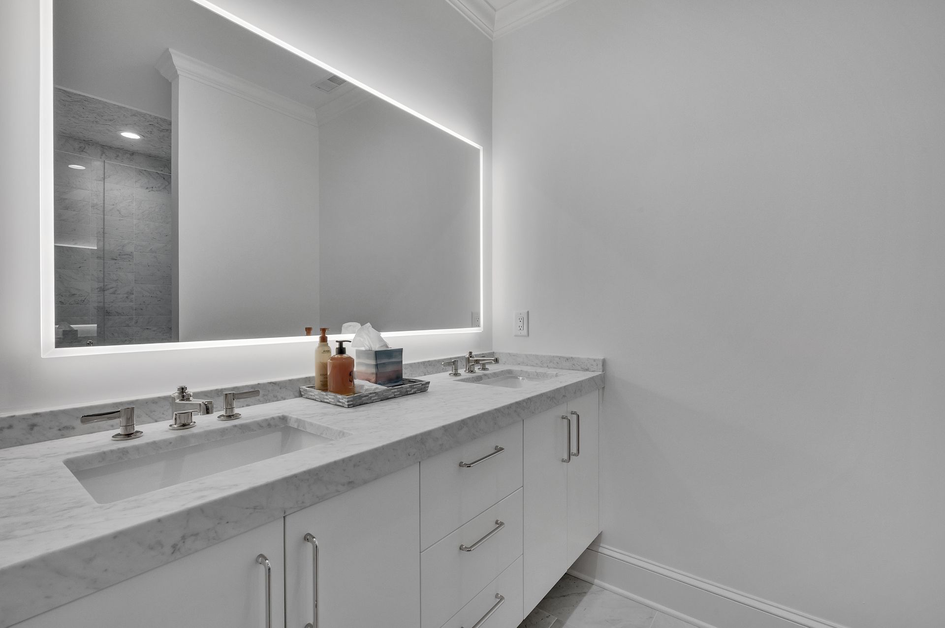 Modern bathroom with marble countertop, illuminated mirror, and white cabinets.