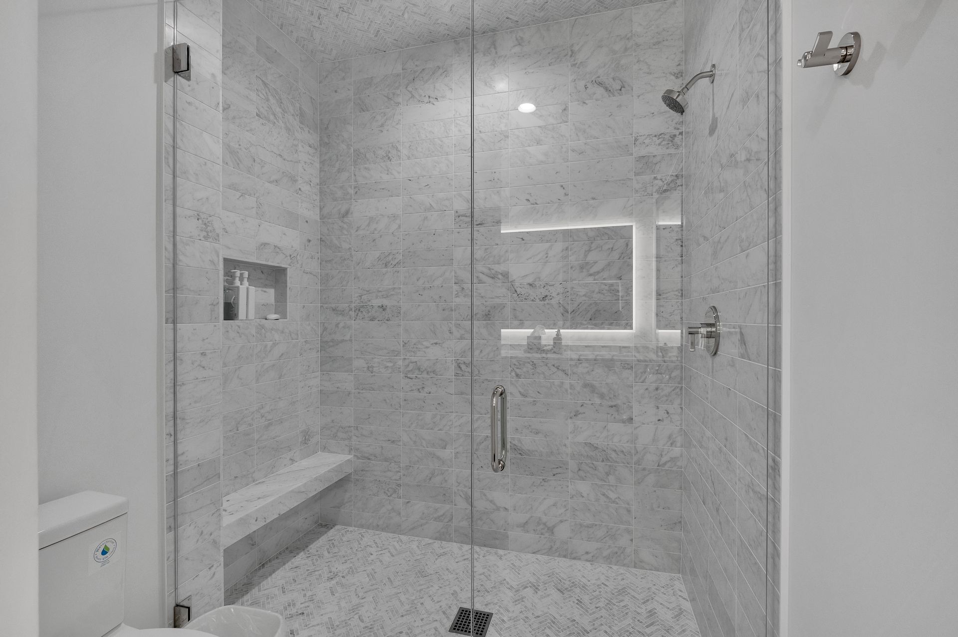 Shower stall with glass doors, gray stone tile, built-in bench, and chrome fixtures.