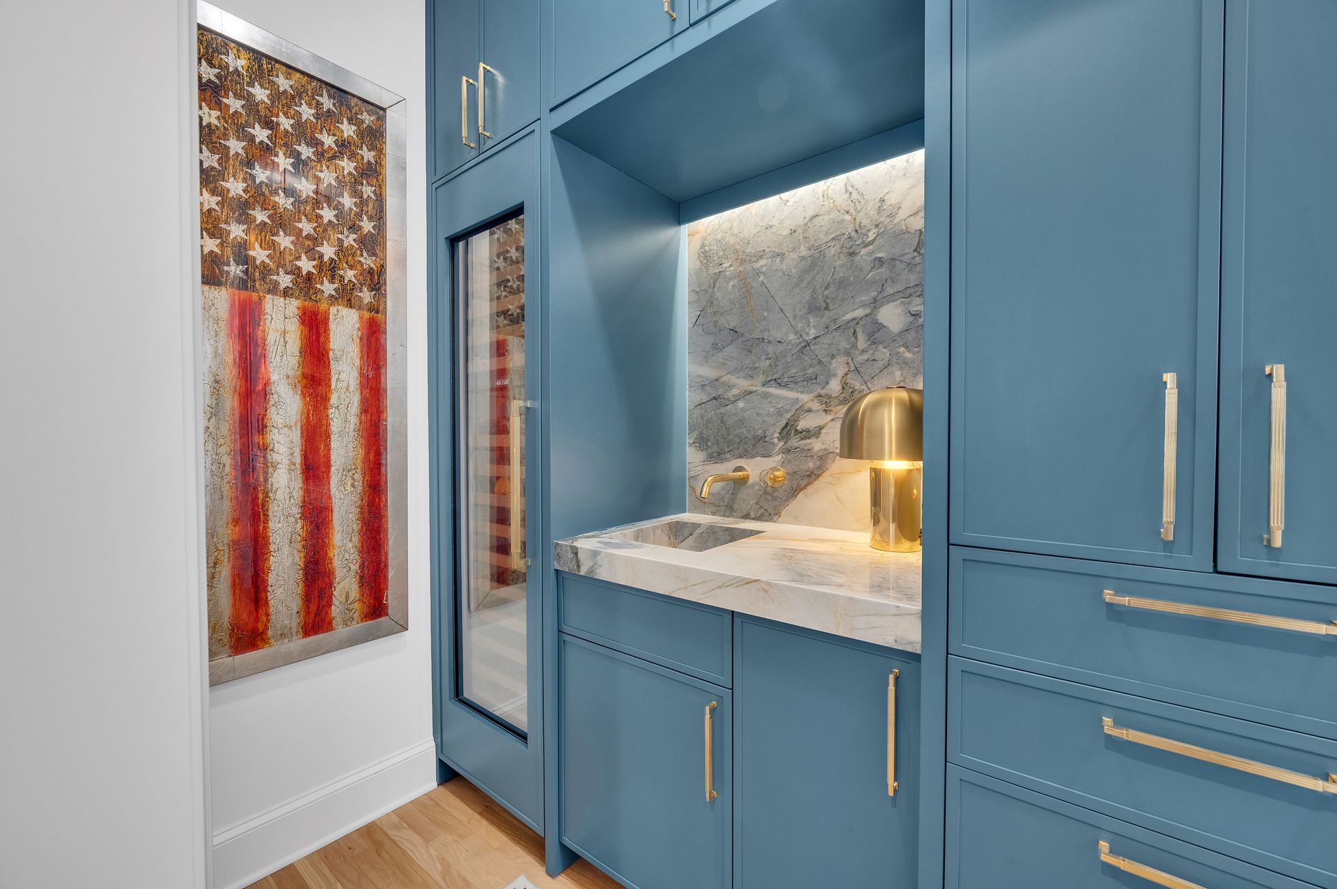 Blue built-in cabinet with marble countertop and a small sink, next to a framed American flag artwork.