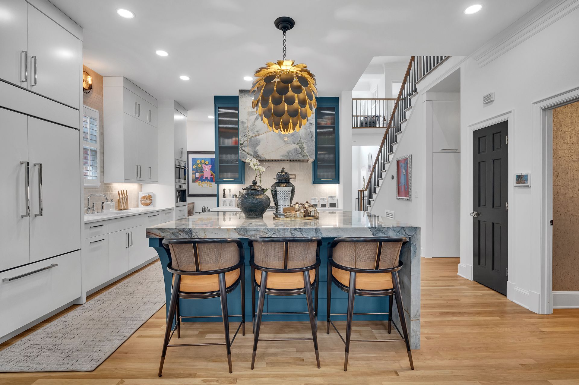 Modern kitchen with blue island, white cabinets, gold light fixture, and wooden floors.