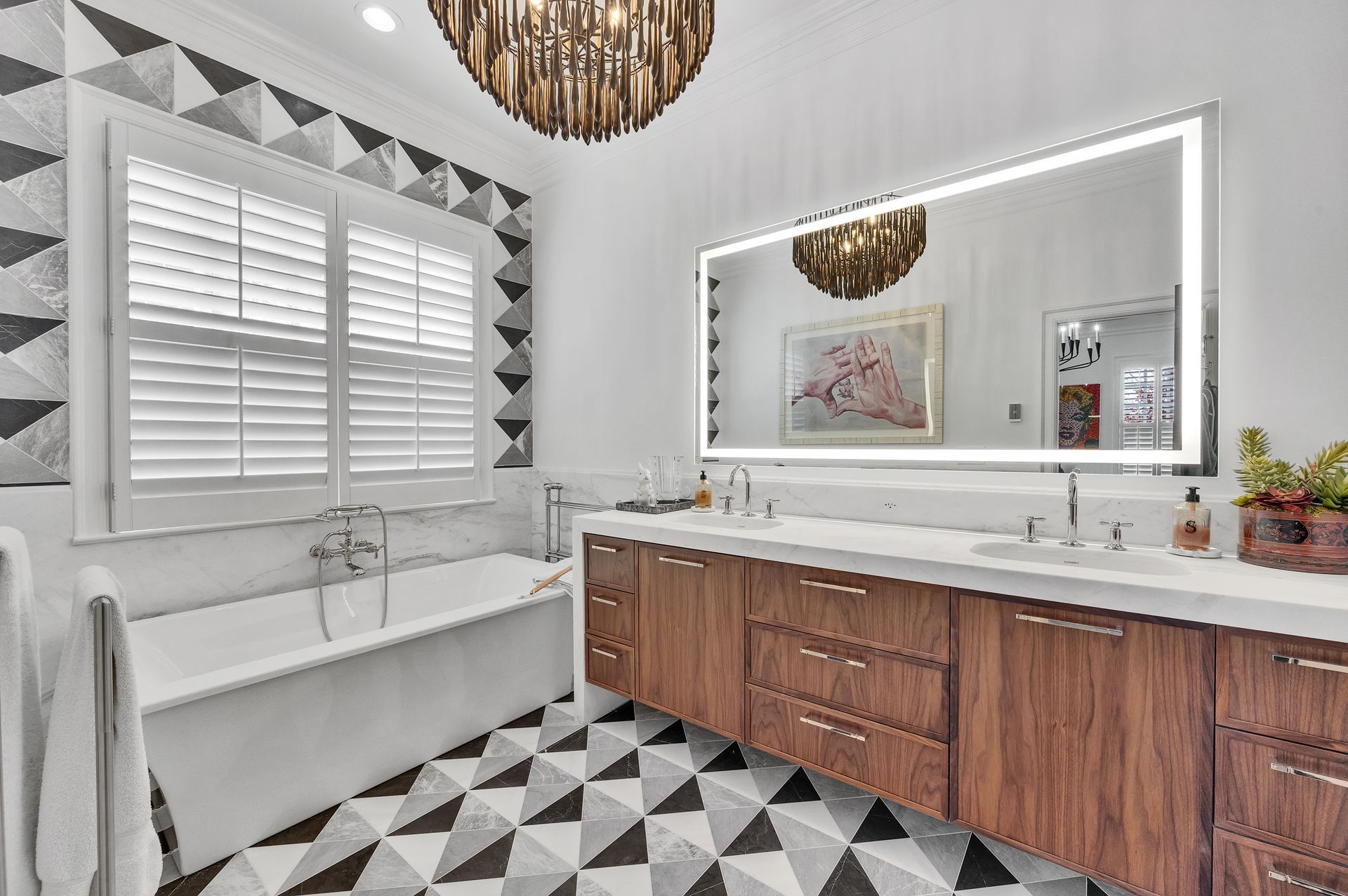 Luxury bathroom with geometric tile, wood vanity, bathtub, and large lighted mirror.