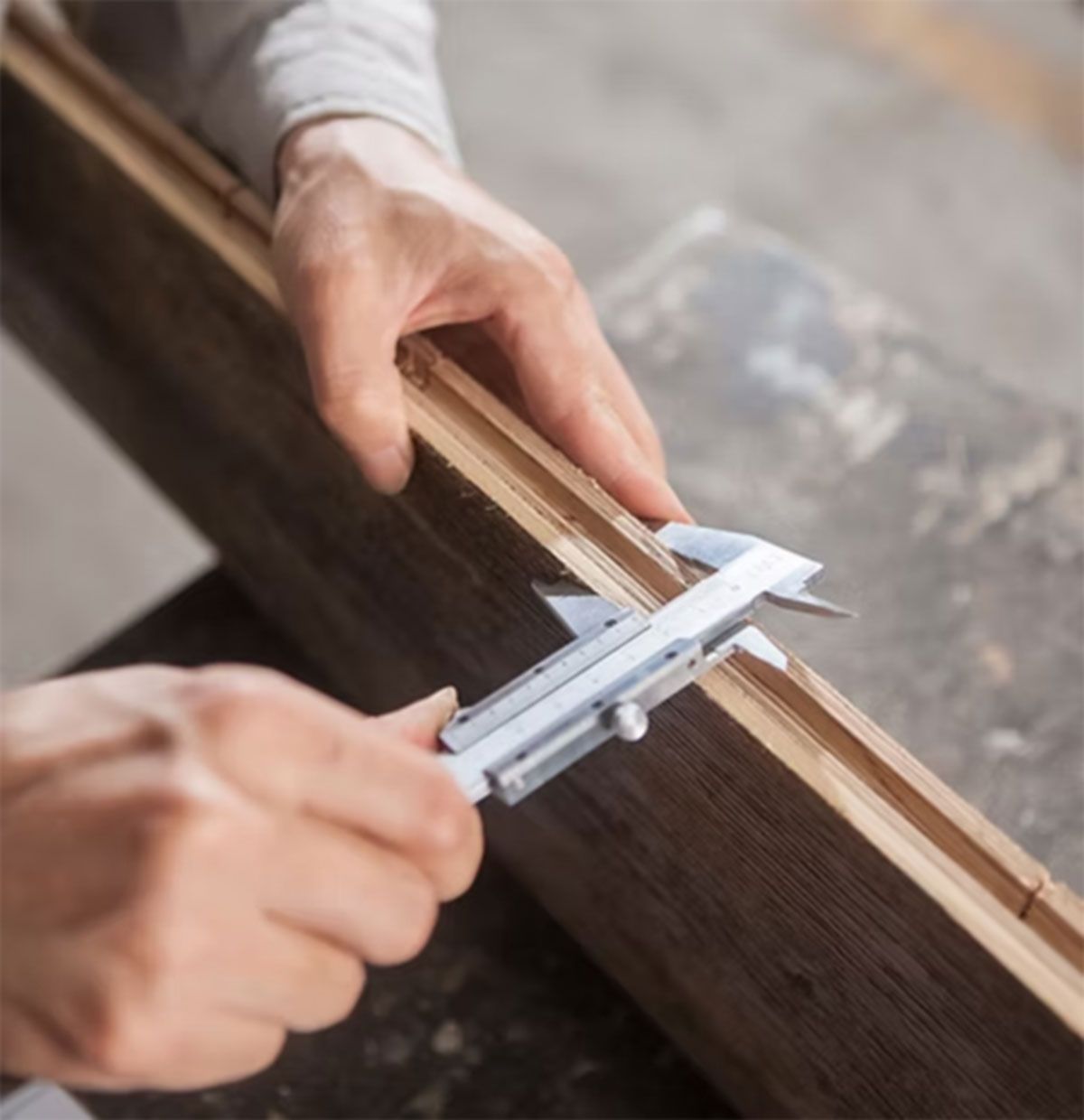 Hands measuring a wooden frame with calipers on a workshop table