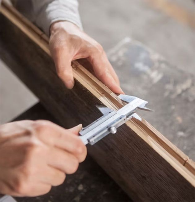 Hands measuring a wooden frame with calipers on a workshop table