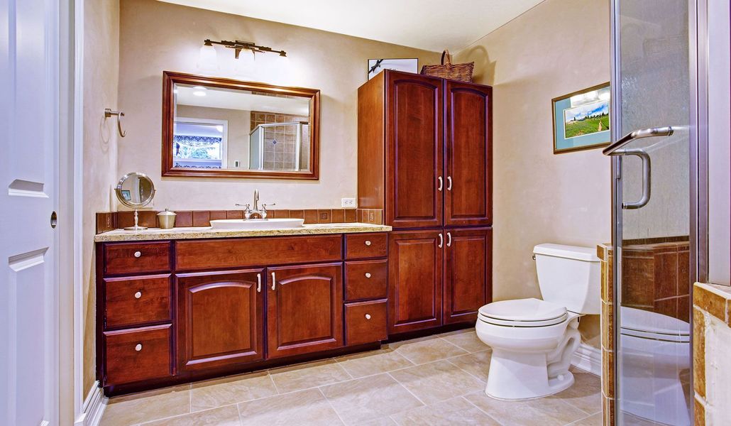 Spacious bathroom with wood vanity, large mirror, toilet, and glass-enclosed shower.