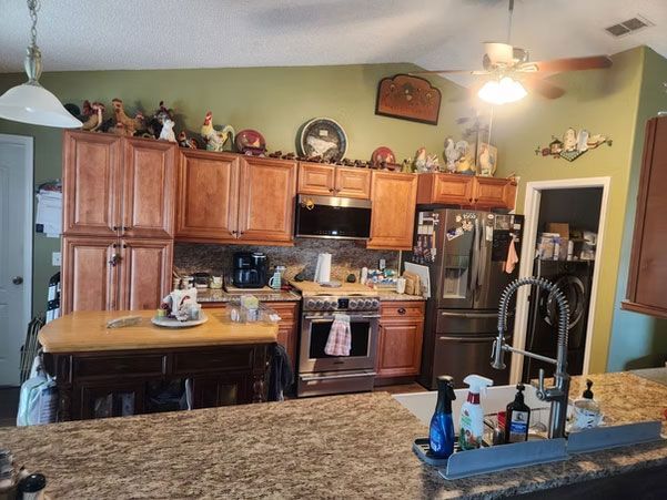 Kitchen with wooden cabinets, stainless appliances, granite island, and decorative items above the cupboards.