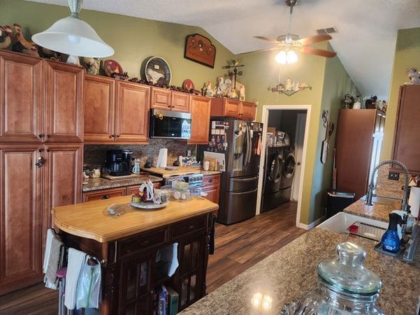 Kitchen with wooden cabinets, black appliances, island table, and granite countertop in a warm, cluttered home interior