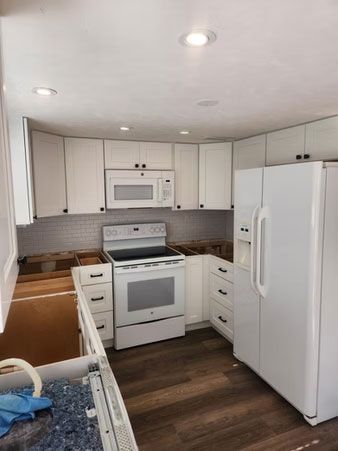 Bright white kitchen with stove, microwave, refrigerator, and wood floors