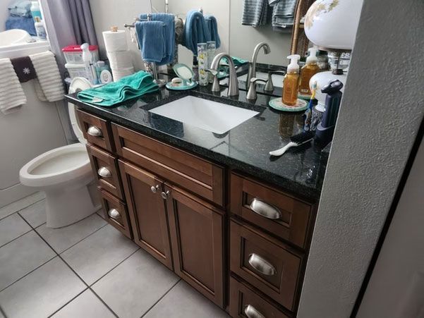 Bathroom vanity with dark wood cabinets, black countertop, sink, mirror, and toiletries.