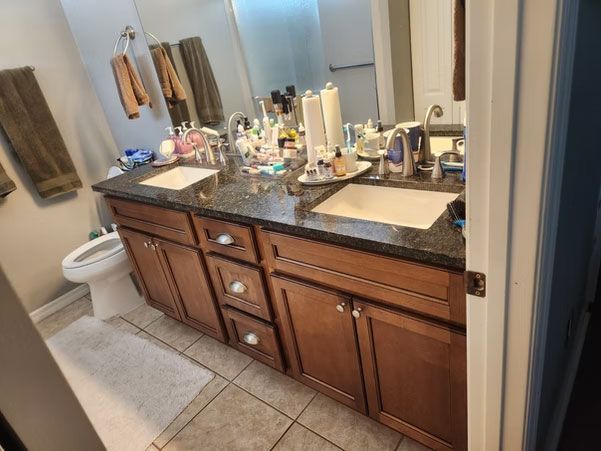 Bathroom vanity with dark wood cabinets, granite countertop, sinks, mirror, and toiletries.