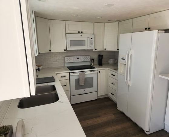 Bright white kitchen with white cabinets, appliances, and dark wood floor