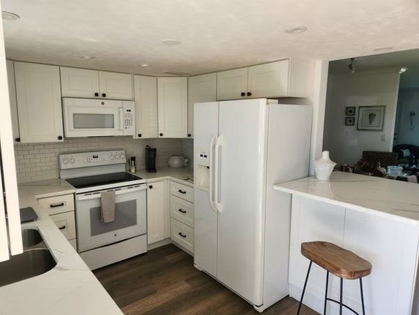 Bright white kitchen with white appliances, dark wood floor, and a breakfast bar with stools
