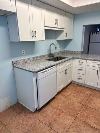 Small kitchen with white cabinets, speckled countertops, sink, dishwasher, and tan tile floor.