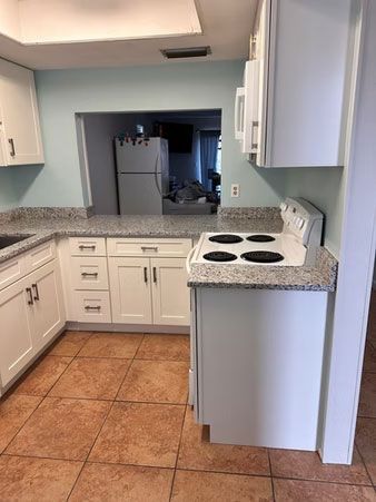Small kitchen with white cabinets, speckled countertops, terracotta tile floor, and a white electric stove.