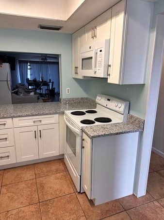 Small kitchen with white cabinets, white stove and microwave, and speckled countertops leading to a dining area.